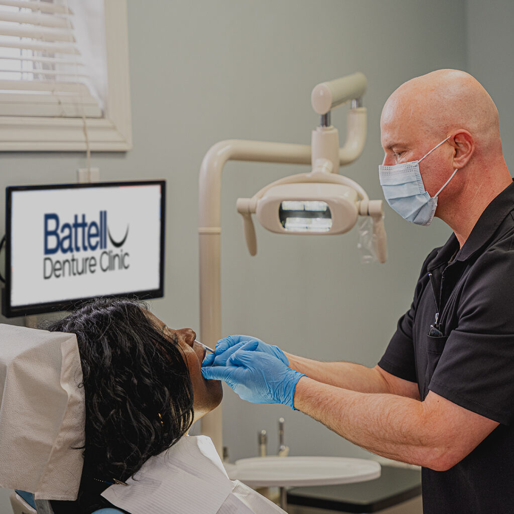 Patient at Battell Denture Clinic in Hamilton sitting in the exam chair receiving a denture exam from Michael Battell.