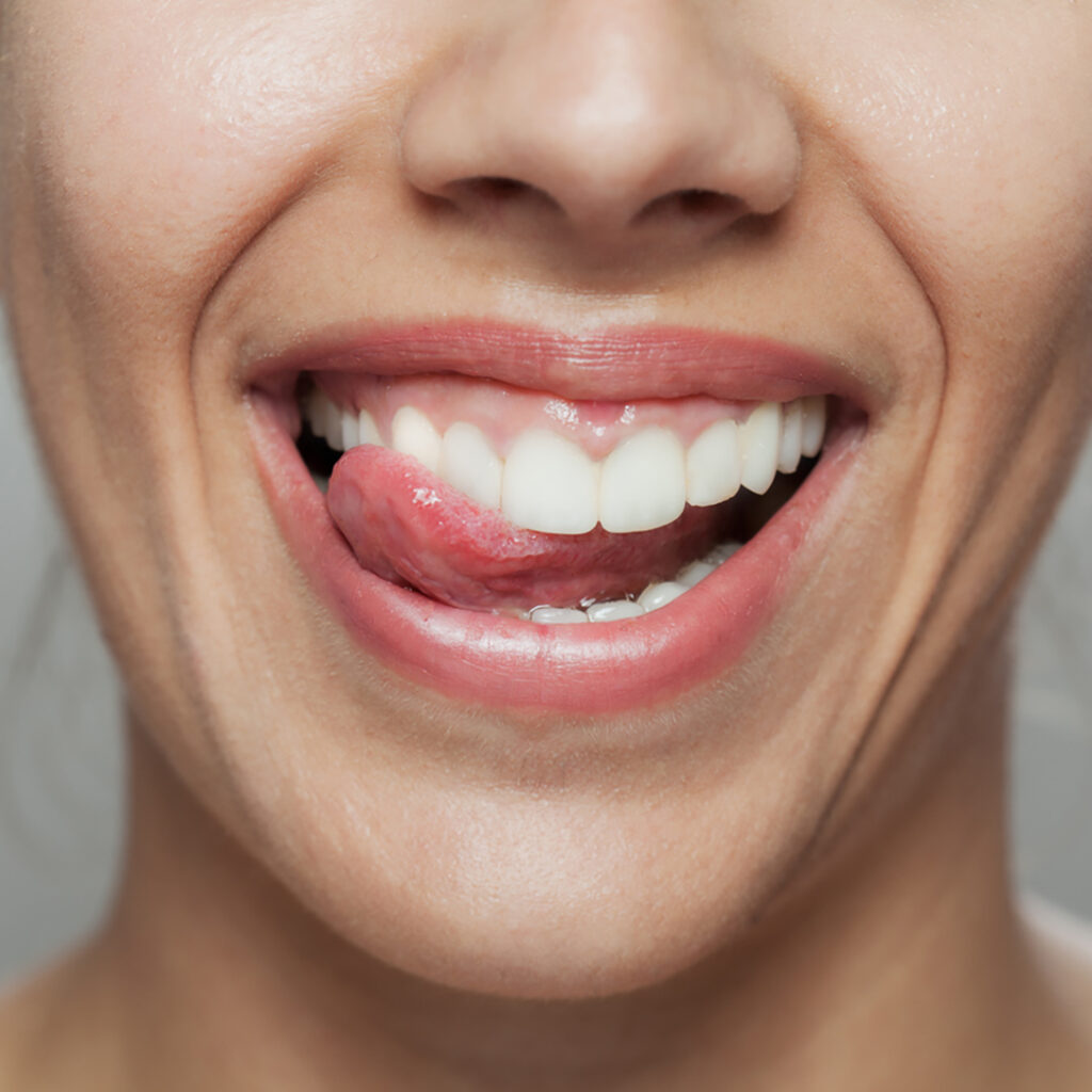 Stock photo of a woman smiling, sliding her tongue along her upper teeth