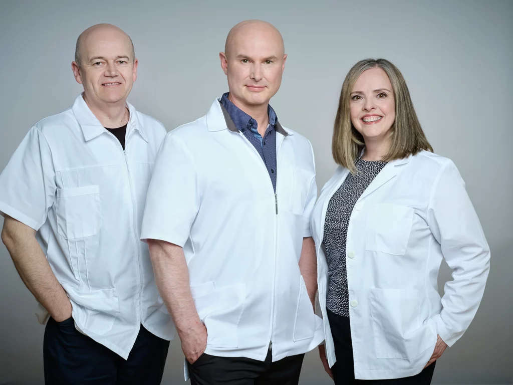 Pavlo, Michael Battell, and Trish standing side by side smiling in white lab coats.