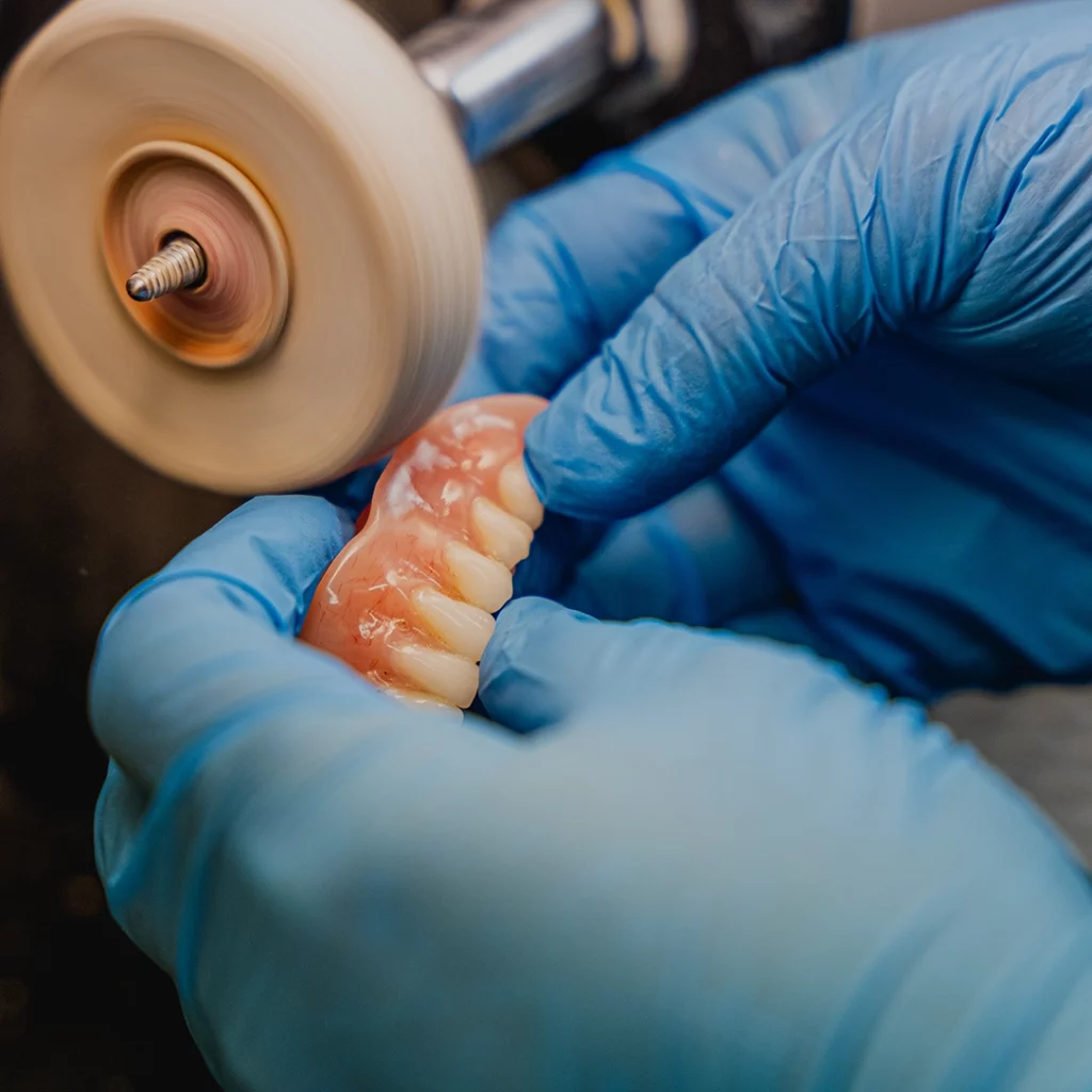 Indistinguishable person in blue latex gloves working on a pair of upper, complete dentures.