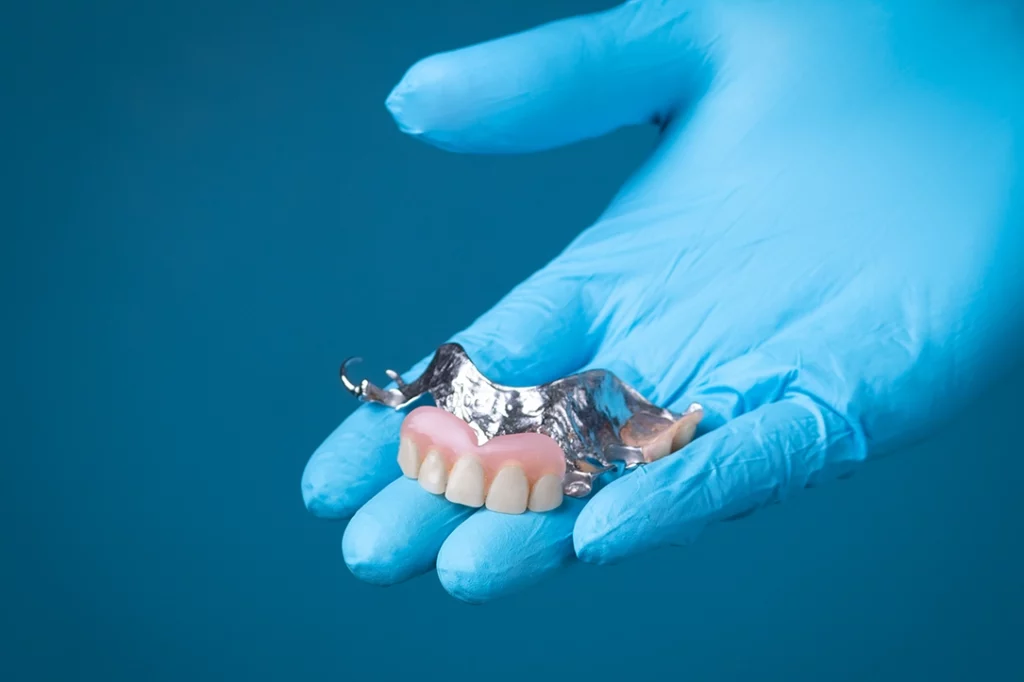 Undisguishable person holding a partial denture in the palm of their hand.